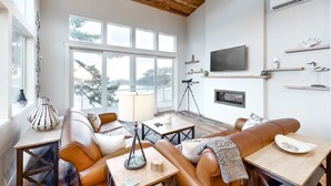 Een moderne woonkamer met lederen banken, een houten plafond, grote ramen en een flatscreen televisie aan de muur.