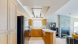 Une cuisine moderne avec des meubles en bois, un réfrigérateur noir et une cheminée en pierre.