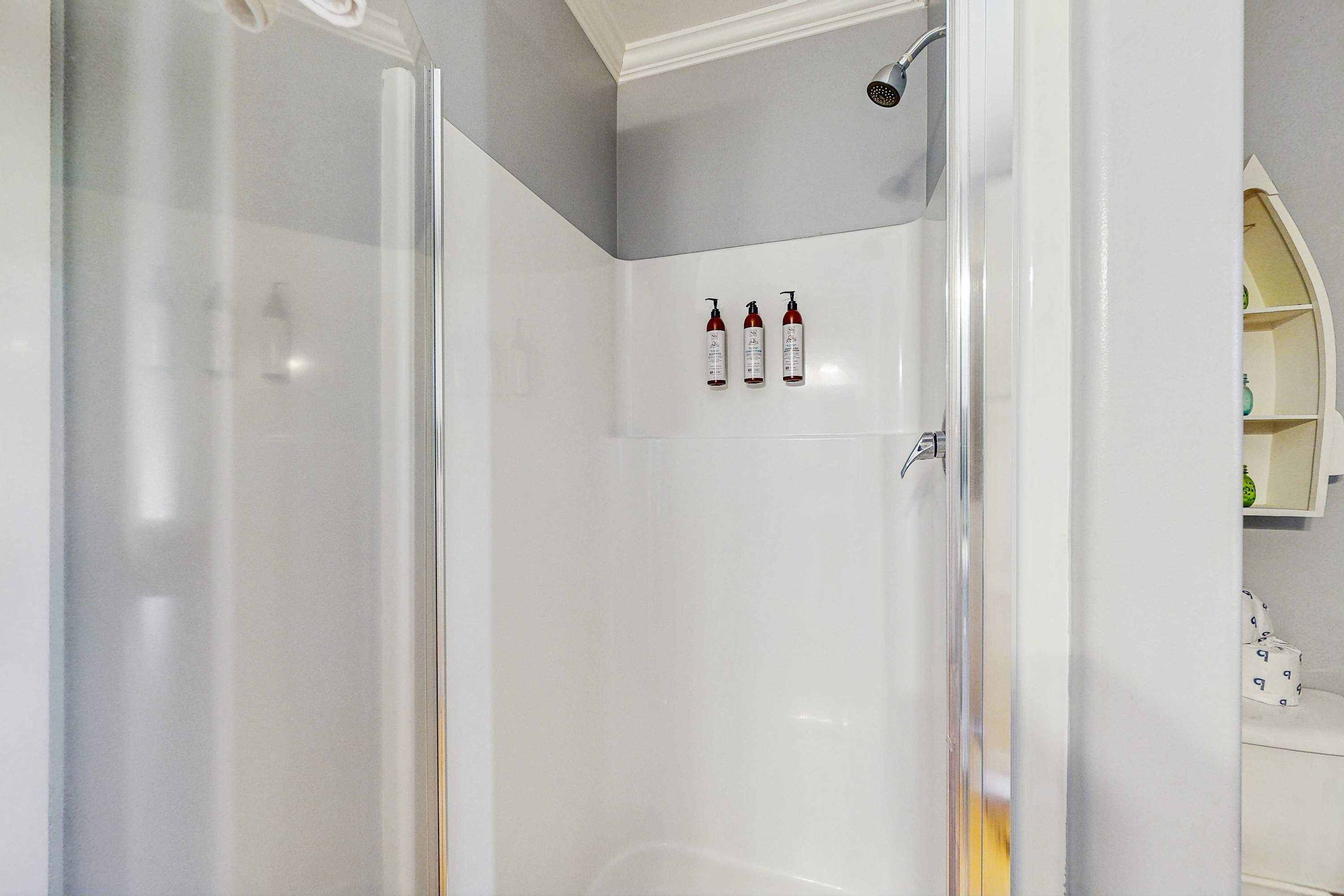 Un bagno moderno con cabina doccia in vetro, una vasca da bagno bianca e tre flaconi di shampoo a parete.