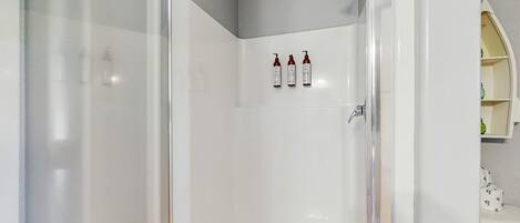 Un bagno moderno con cabina doccia in vetro, una vasca da bagno bianca e tre flaconi di shampoo a parete.