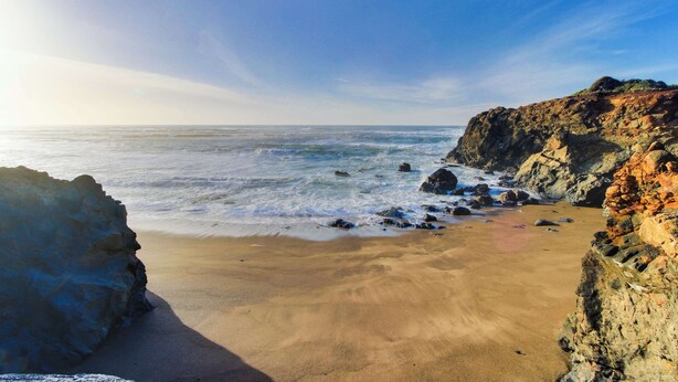 Ein Strand mit Felsformationen und ruhigen Wellen.