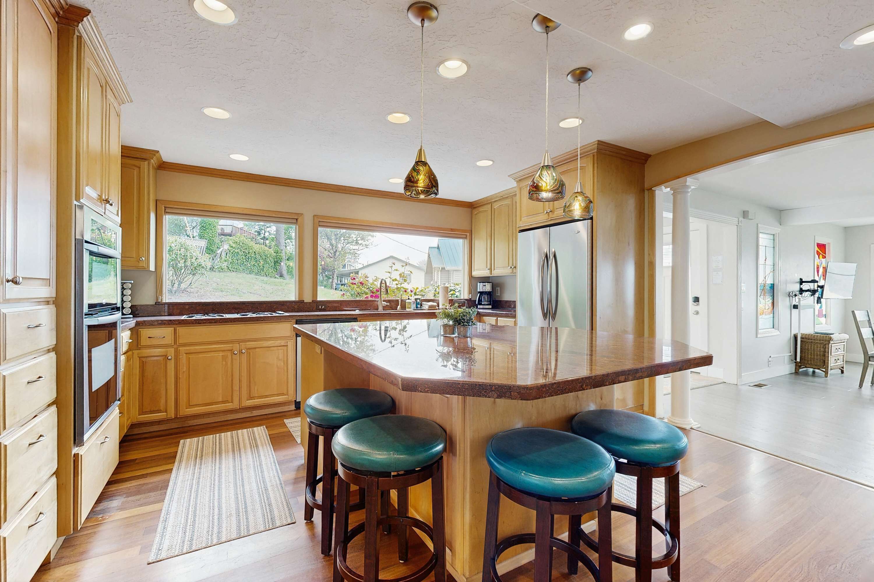 Una cocina amplia con armarios de madera, una isla grande con taburetes de bar, electrodomésticos de acero inoxidable e iluminación colgante.