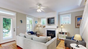 A living room with a fireplace, a ceiling fan, and a TV mounted above it. - Bella Beach Home with private hot tub walk to beach park and cafe (Depoe Bay)
