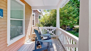 A wooden porch with two Adirondack chairs, a white railing, and a view of a tree-lined street. - Bella Beach Home with private hot tub walk to beach park and cafe (Depoe Bay)