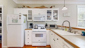 A compact kitchen with white cabinets, a refrigerator, a stove, a microwave, and a sink. - Bella Beach Home with private hot tub walk to beach park and cafe (Depoe Bay)