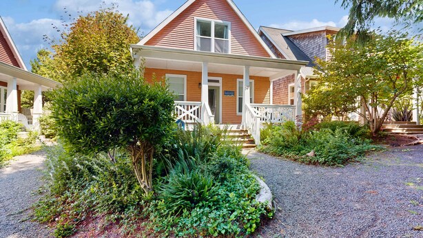 A two-story house with a porch, surrounded by lush greenery and a gravel driveway. - Bella Beach Home with private hot tub walk to beach park and cafe (Depoe Bay)