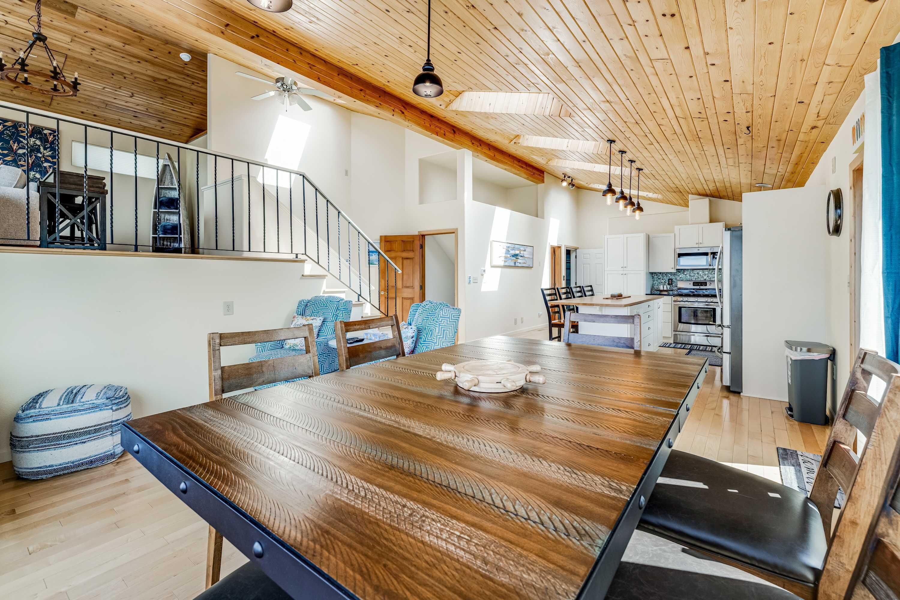A spacious dining area with a wooden table and chairs, a staircase leading to an upper level, and a kitchen in the background.