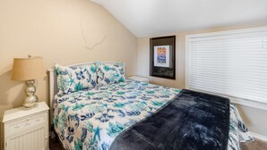 A bedroom with a bed, a nightstand, a lamp, a framed picture on the wall, and a window with blinds. - Ocean view cabin with deck and beach access dog friendly (Depoe Bay)