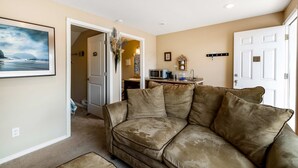 A living room with a beige couch, a painting on the wall, and a door leading to another room. - Ocean view cabin with deck and beach access dog friendly (Depoe Bay)
