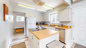 Moderni keittiö, jossa on valkoiset kaapit, puinen työtaso ja sisäänrakennettu mikroaaltouuni.