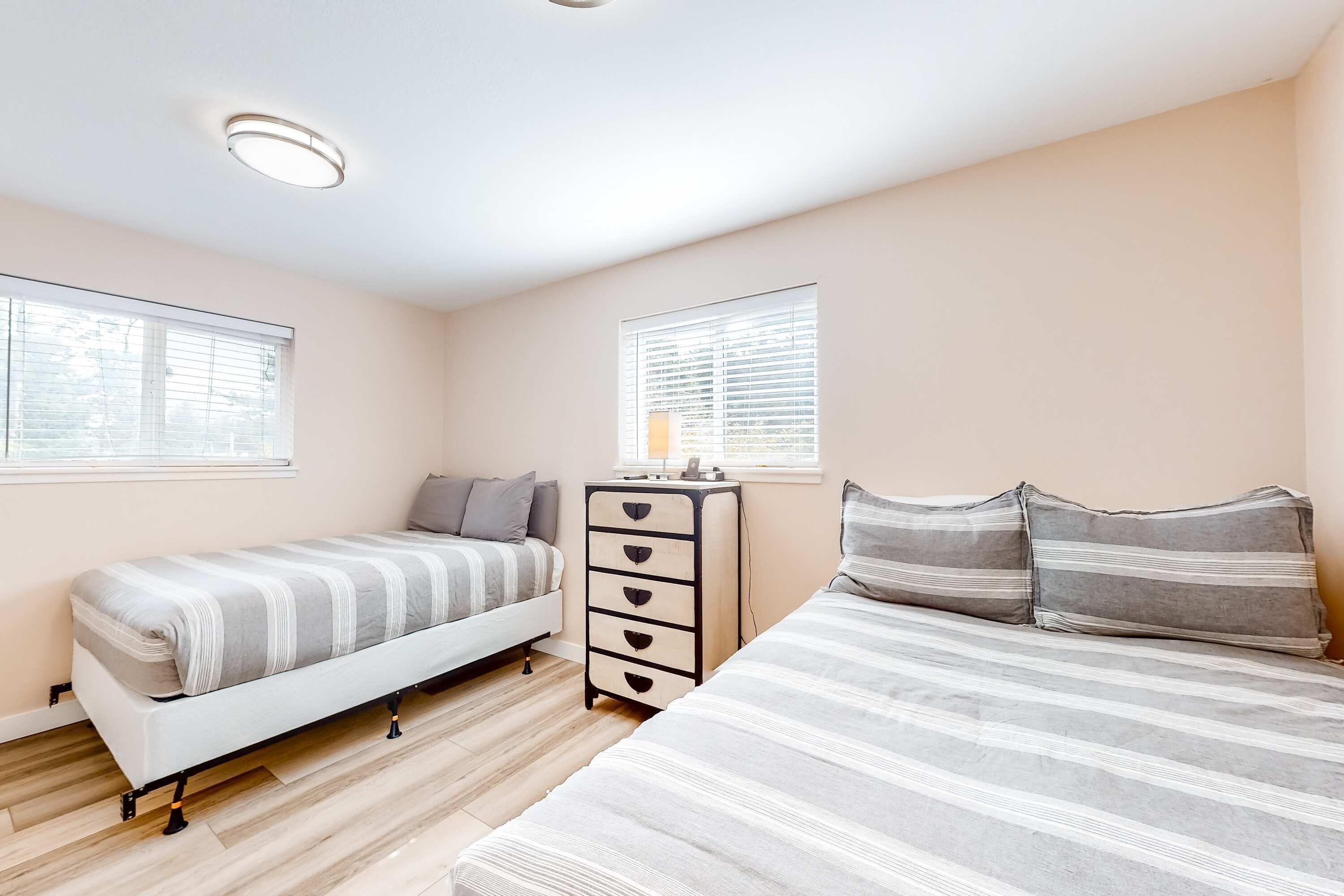 A bedroom with a single bed, a dresser, and two windows.
