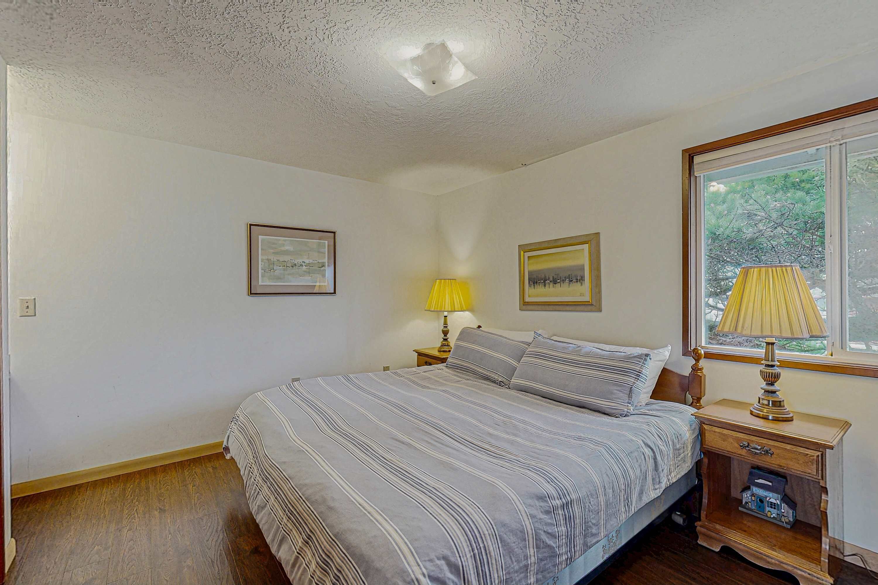 A bedroom with a bed, two bedside tables, a window with a view, and two framed pictures on the wall.