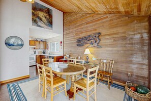 A dining area with a wooden table and chairs, a wooden accent wall, and a kitchen in the background. - Dog friendly home with oceanfront location and fireplace walk to the beach (Gleneden Beach)