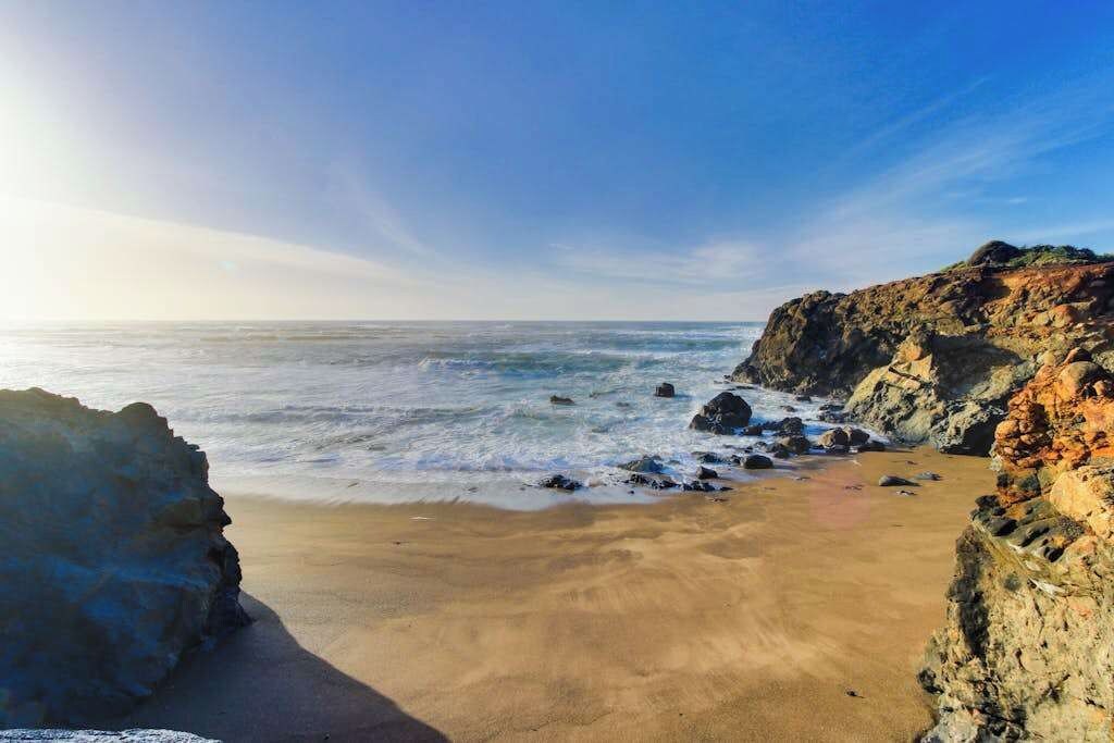 A coastal landscape with a sandy beach, rocky outcrops, and the ocean.