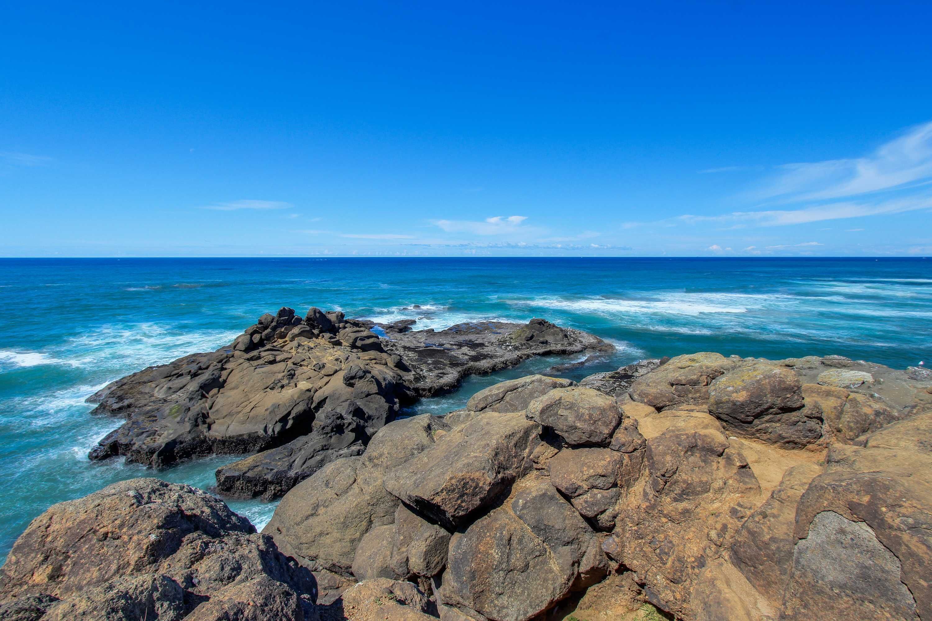 Une côte rocheuse où les vagues s’écrasent contre les rochers, sous un ciel bleu dégagé.