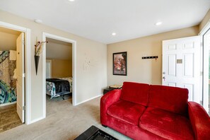 Ein Wohnzimmer mit einem roten Sofa, beige Wänden und einer Tür zu einem weiteren Raum.