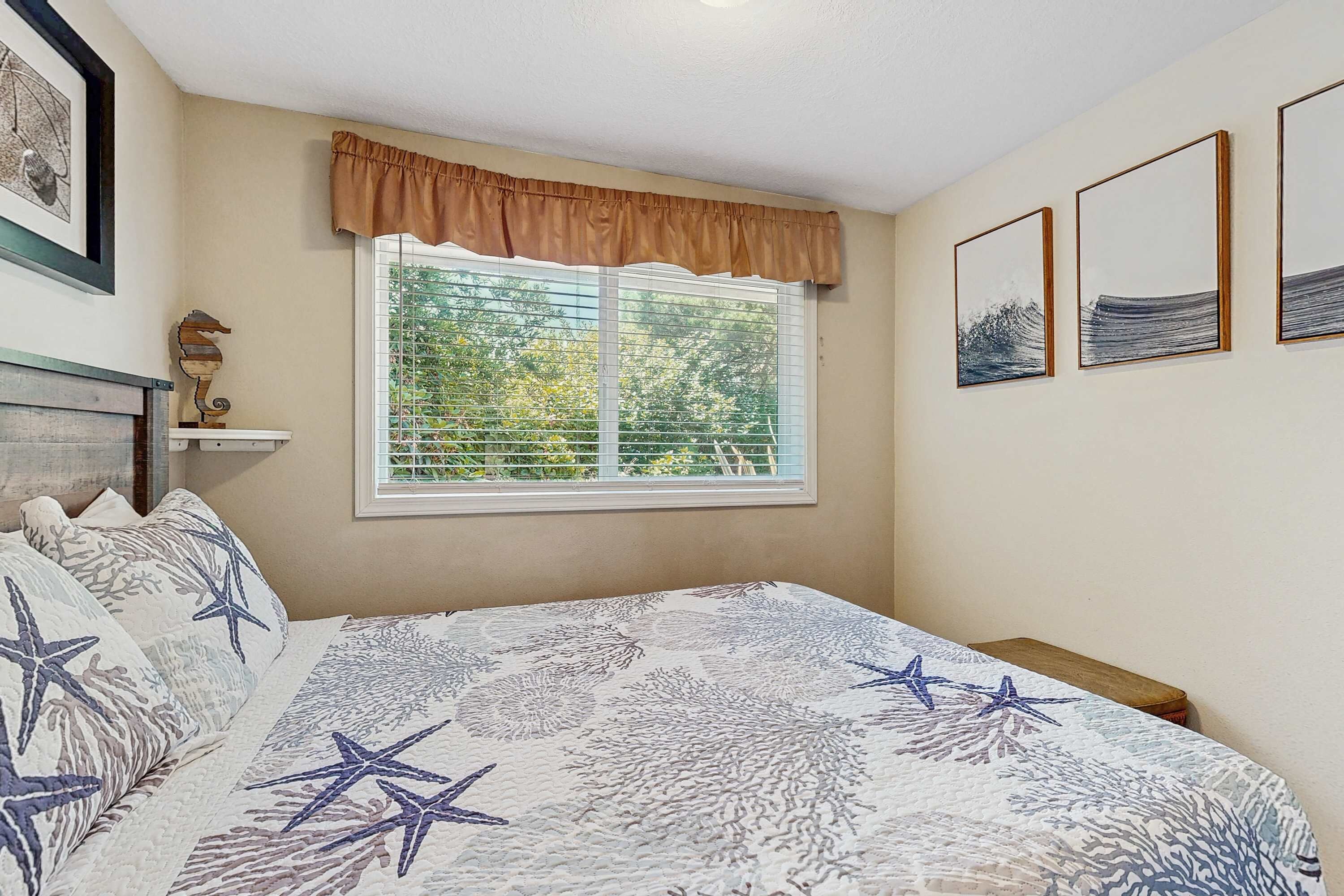 Ein Schlafzimmer mit einem Bett, einem Fenster mit Blick auf Bäume und gerahmten Bildern an der Wand.