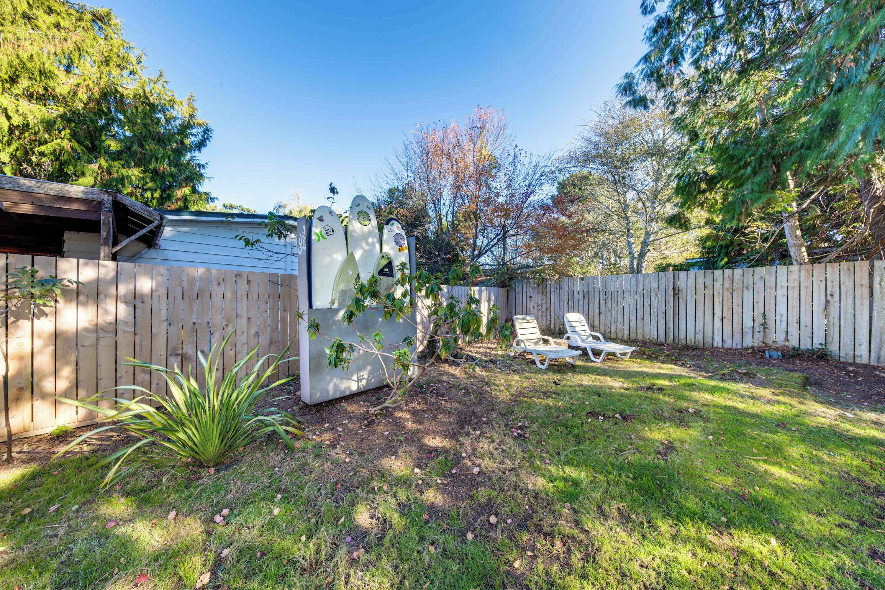 A backyard with a wooden fence, a small garden, and two white lawn chairs.