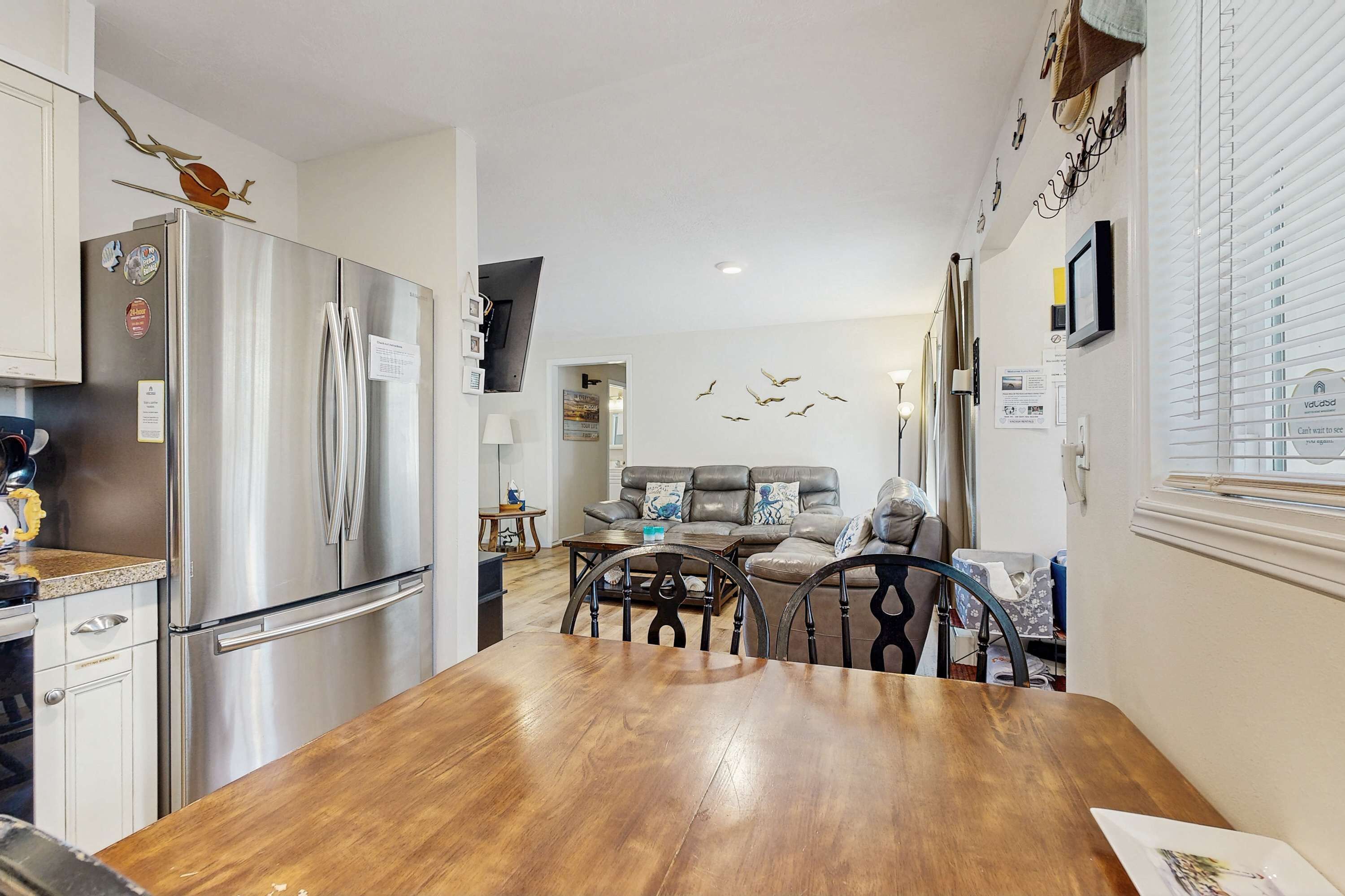A modern kitchen with a stainless steel refrigerator, wooden dining table, and a living area with a sofa and decorative wall art.