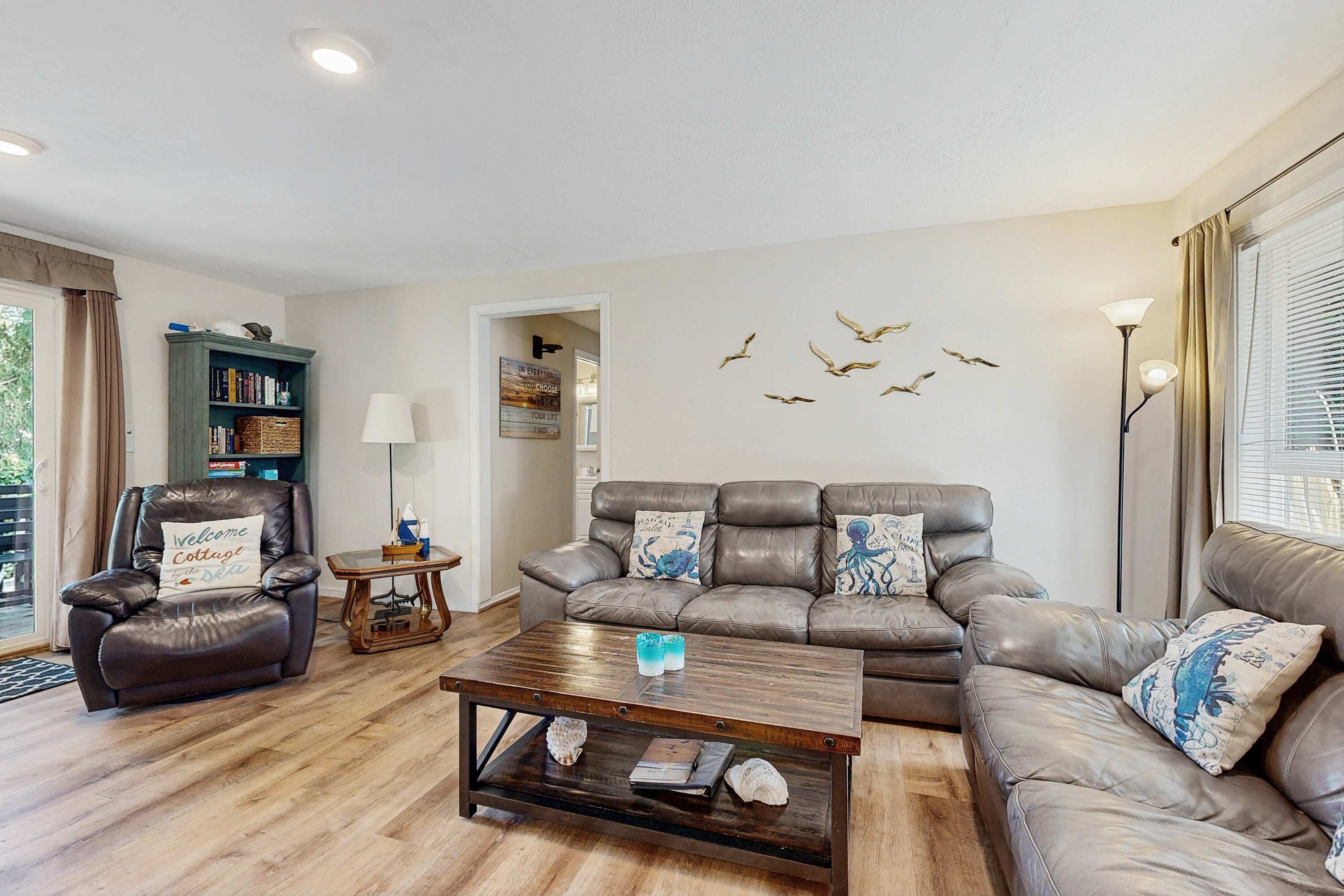 A living room with a leather sofa, a coffee table, a bookshelf, and a wall with bird decals.