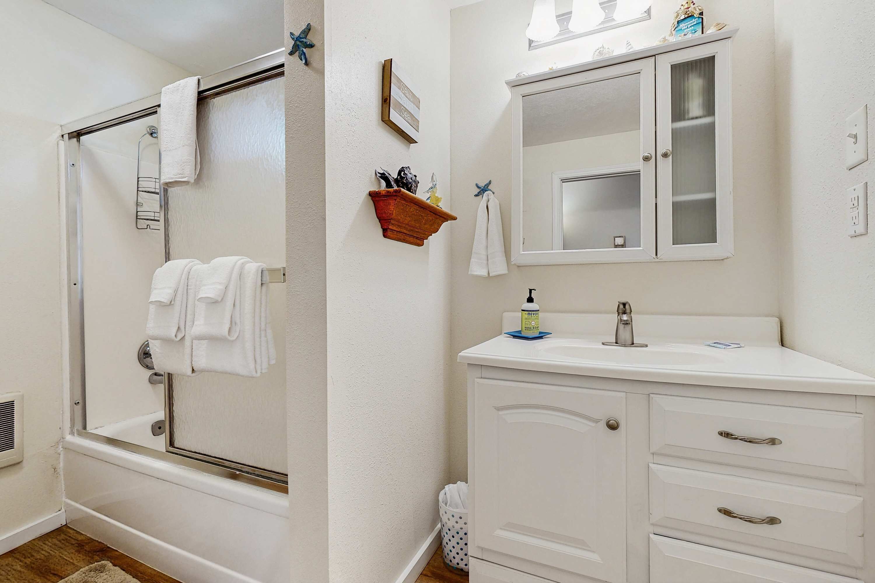 Een badkamer met een bad, een wastafel met lades, een spiegel en een plank met toiletartikelen.