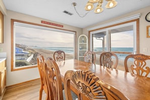 A dining area with a view of the beach, wooden chairs, a large table, and a sign above the windows. - Impressive oceanfront home with great views dog friendly (Gleneden Beach)