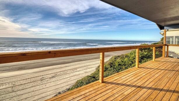 Una terraza de madera con vista al océano y a la playa.
