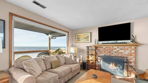 Una sala de estar con un sofá, una mesa de centro, una chimenea, un televisor y vista al océano.
