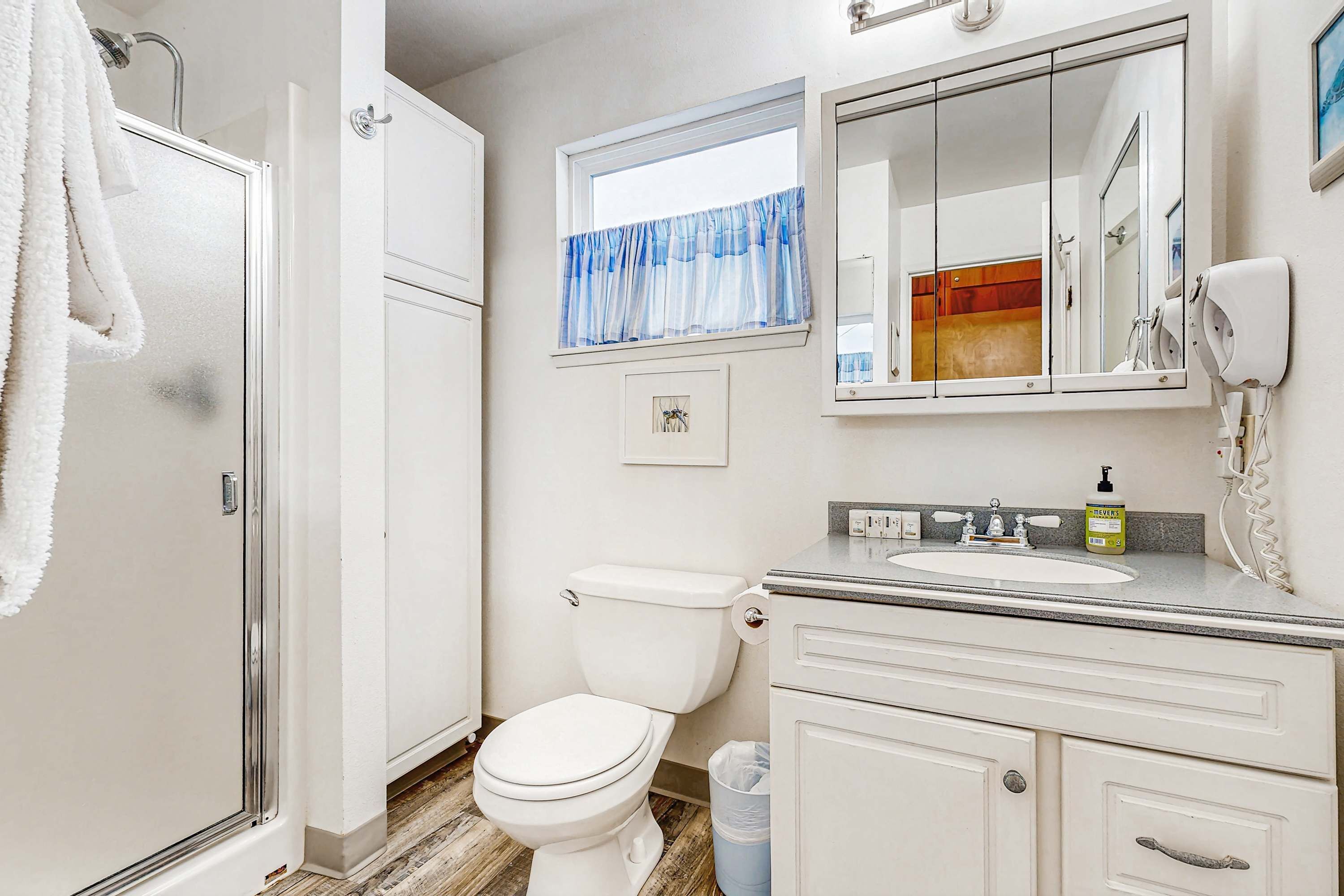 A bathroom with a shower, toilet, vanity, and a large mirror.