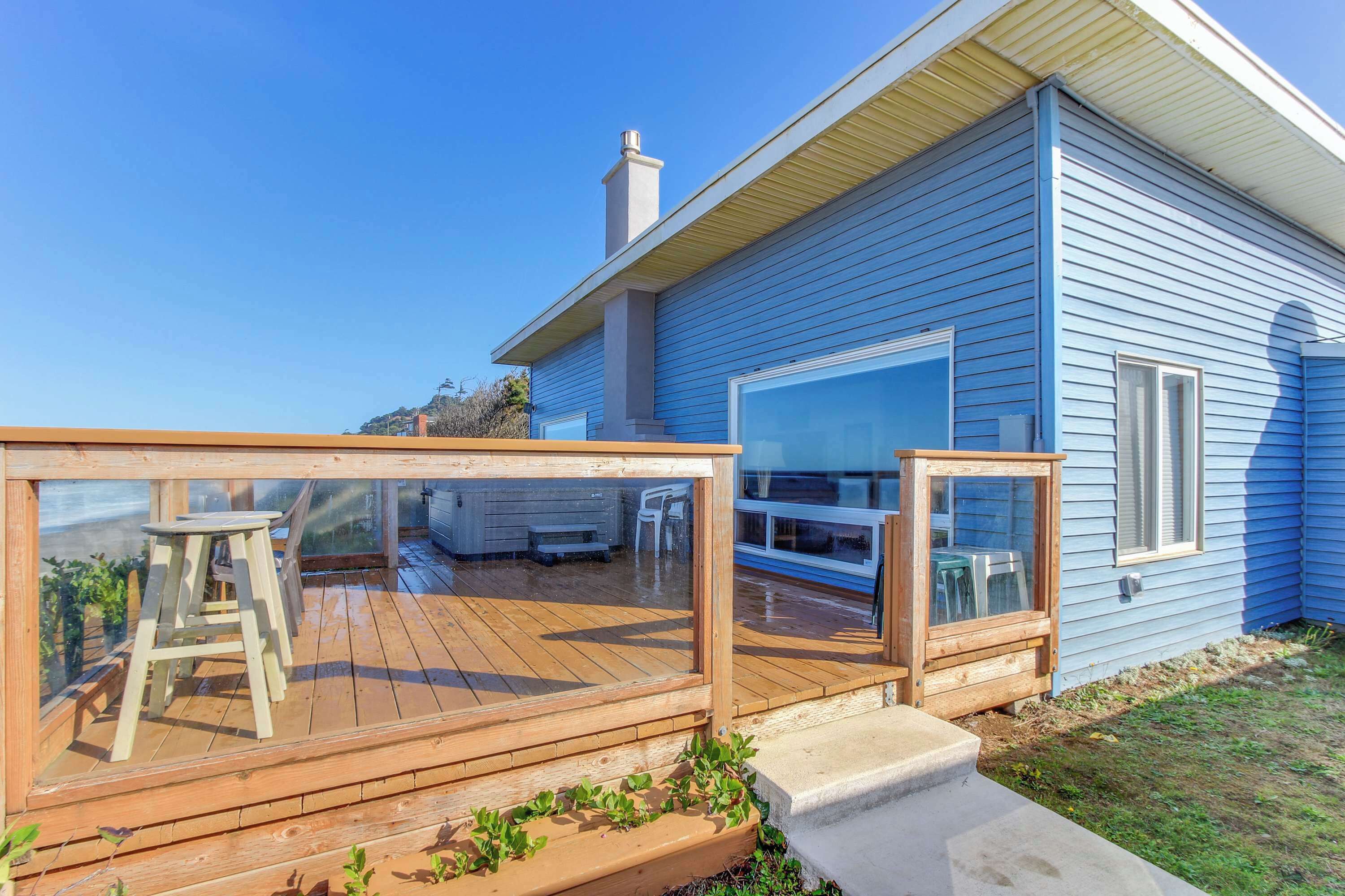 Une maison bleue avec une terrasse en bois, une grande fenêtre et une cheminée.