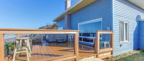 Une maison bleue avec une terrasse en bois, une grande fenêtre et une cheminée.