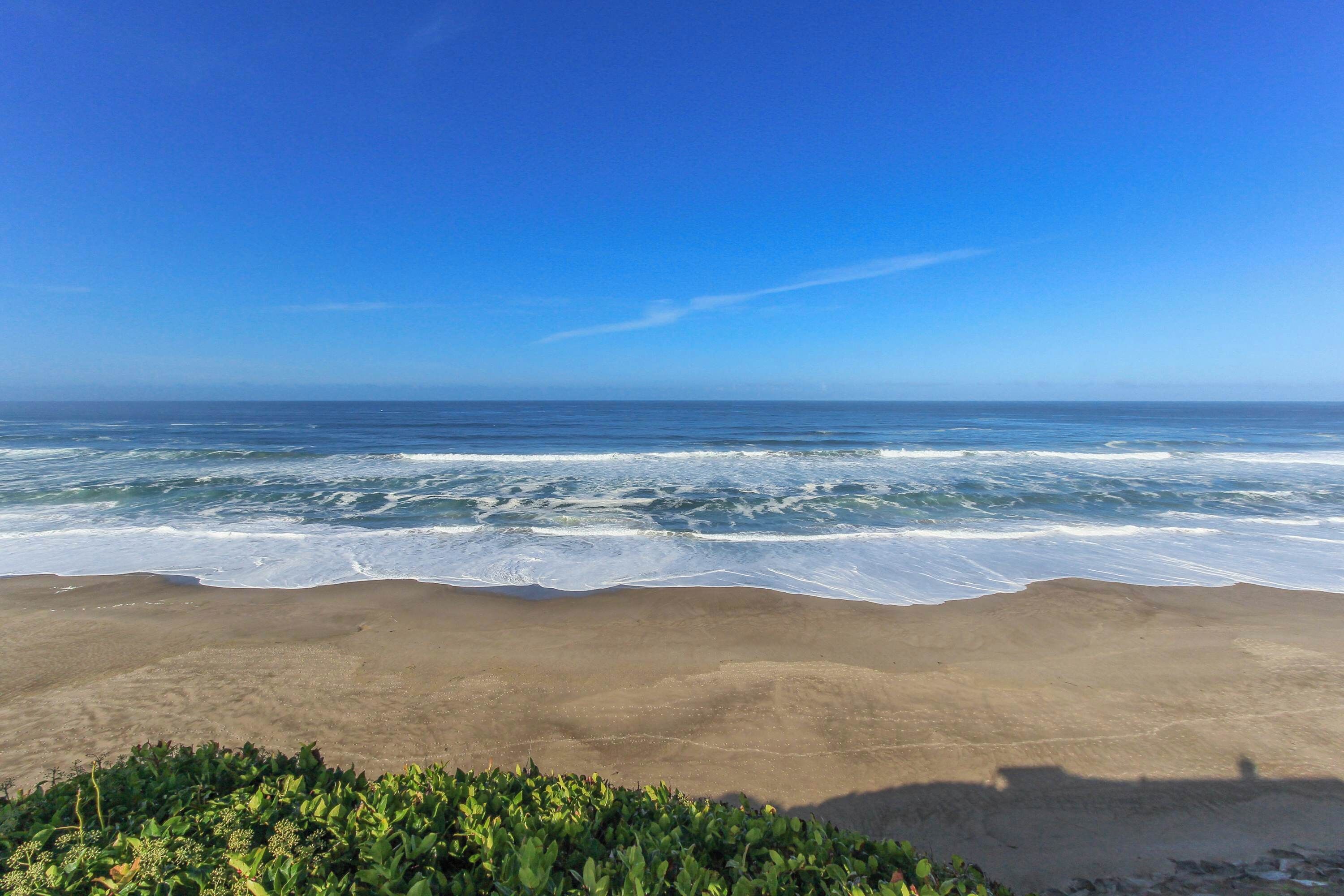 A beach with waves crashing onto the shore and a clear blue sky.