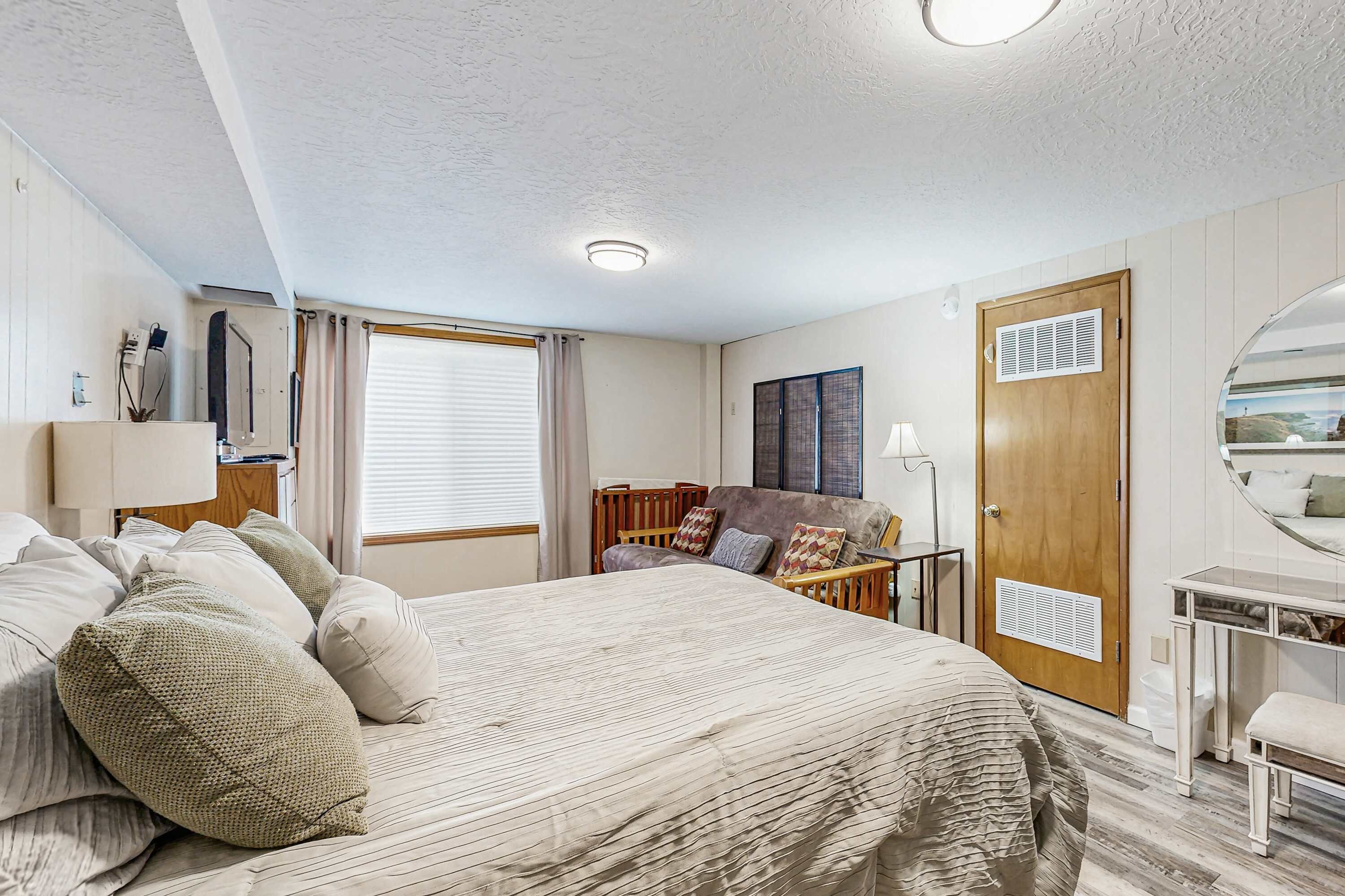 A bedroom with a large bed, a wooden headboard, a bedside table, a mirror, and a window with curtains.