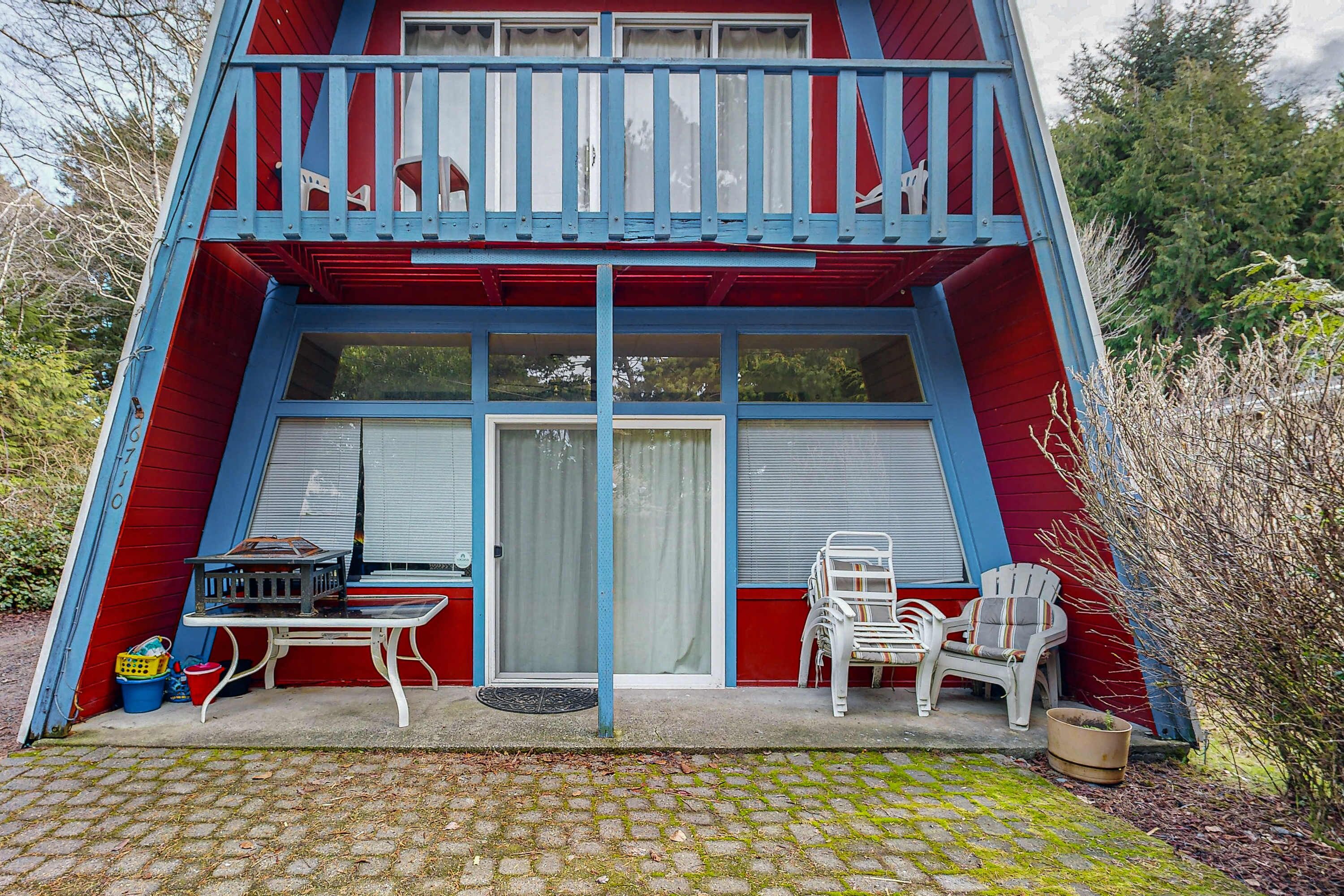Un bâtiment à deux étages, à la façade rouge agrémentée de touches de bleu, doté d’un balcon avec des balustrades blanches, d’une petite table avec des chaises et d’une plante en pot.