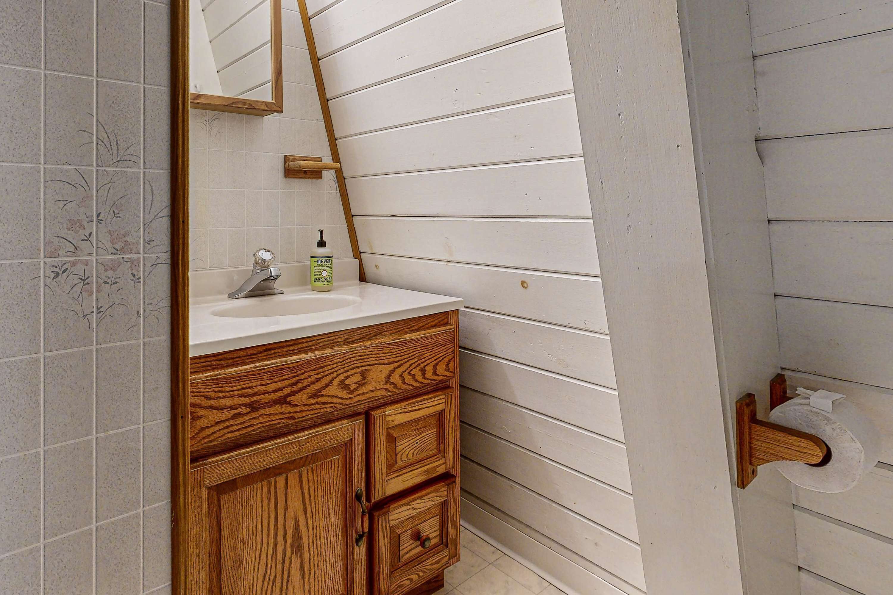 A bathroom with a wooden vanity, a mirror, and a toilet paper holder on the wall.