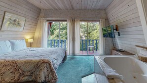 A bedroom with a bed, a bathtub, and a balcony with a view of trees. - Fun and Unforgettable Beach House Dog friendly with a Great Location (Gleneden Beach)