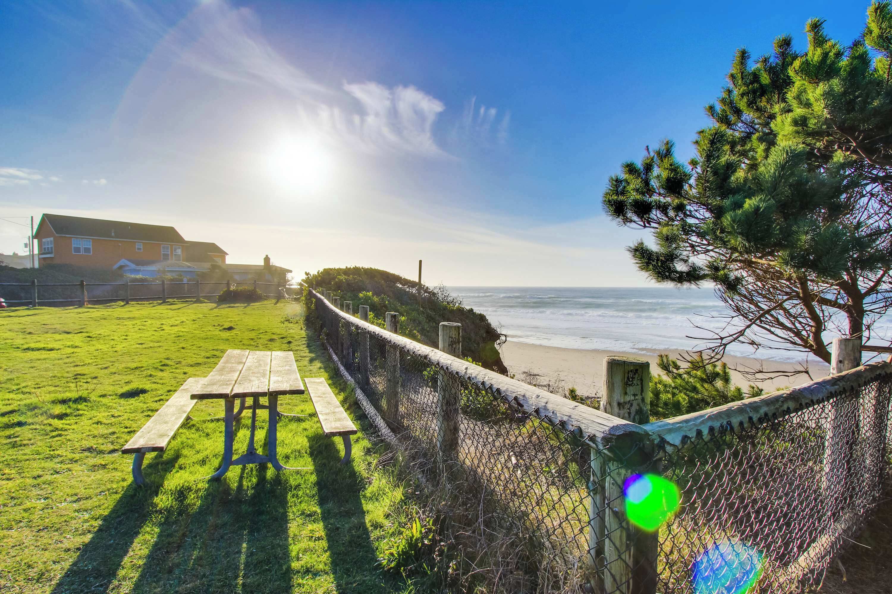 Een picknicktafel en een bank op een gazon met uitzicht op de oceaan en een huis op de achtergrond.