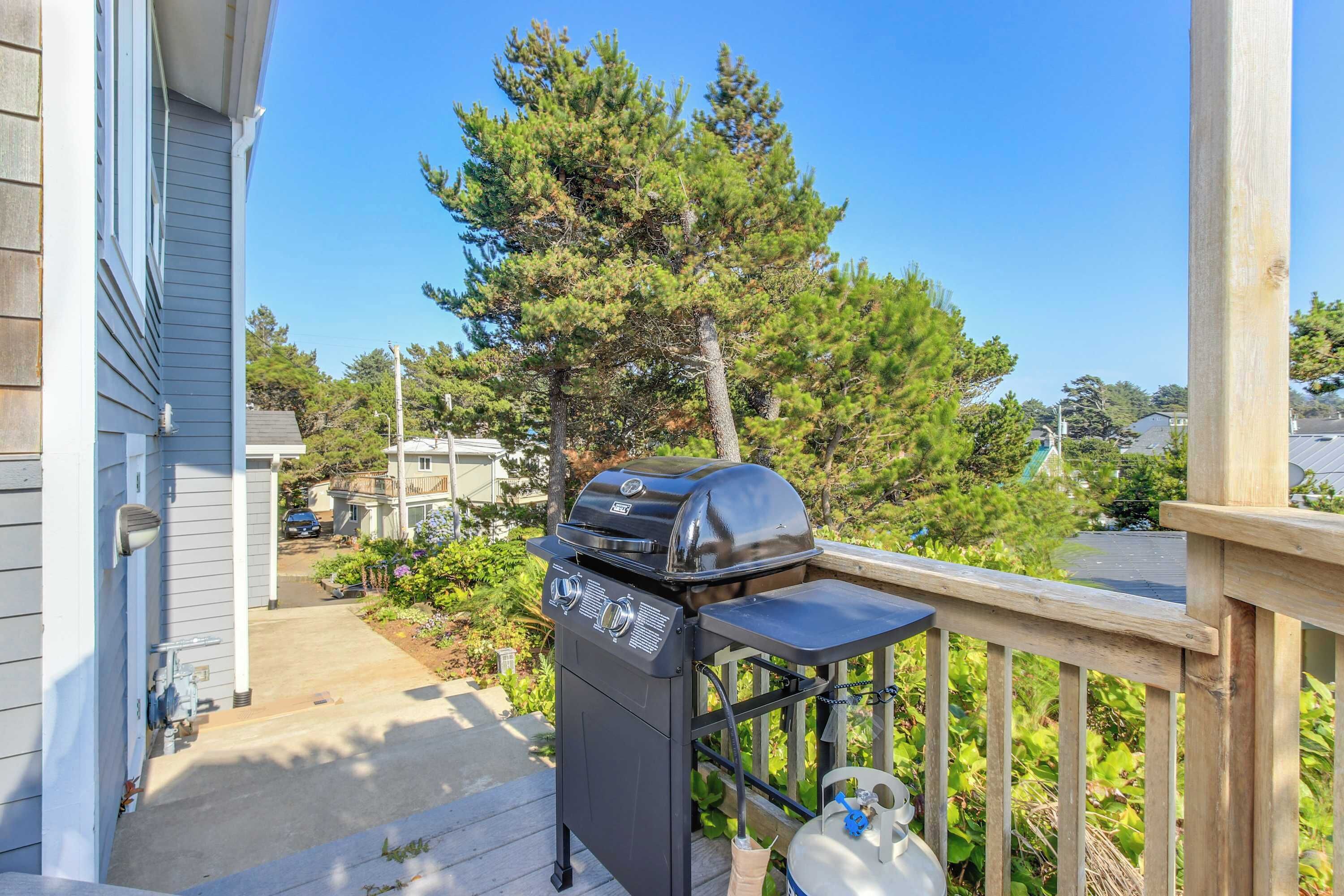 Una parrilla negra de barbacoa en una terraza de madera, con vistas despejadas a un barrio residencial y árboles al fondo.