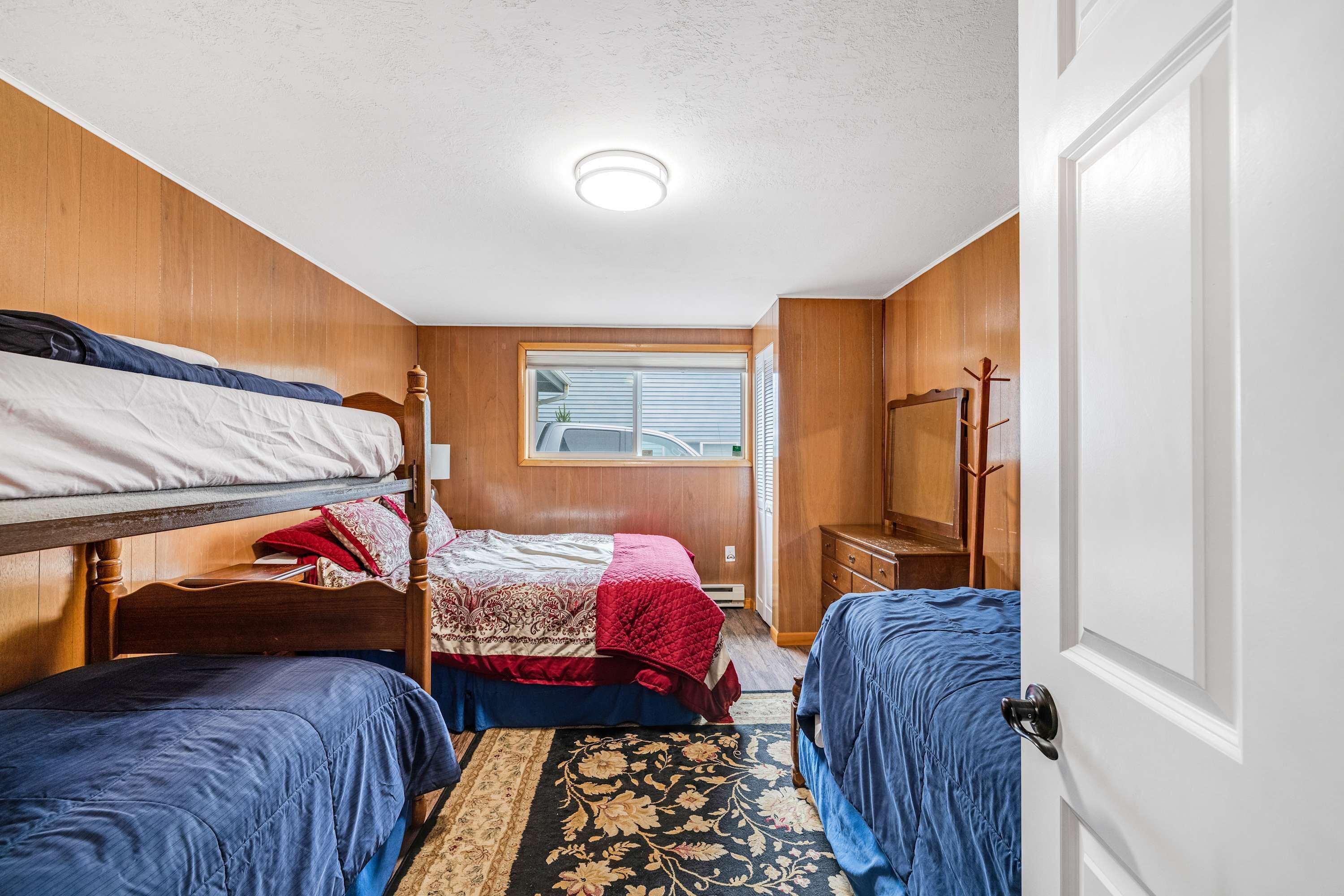 A compact room with bunk beds, a window, a door, and a small dresser.