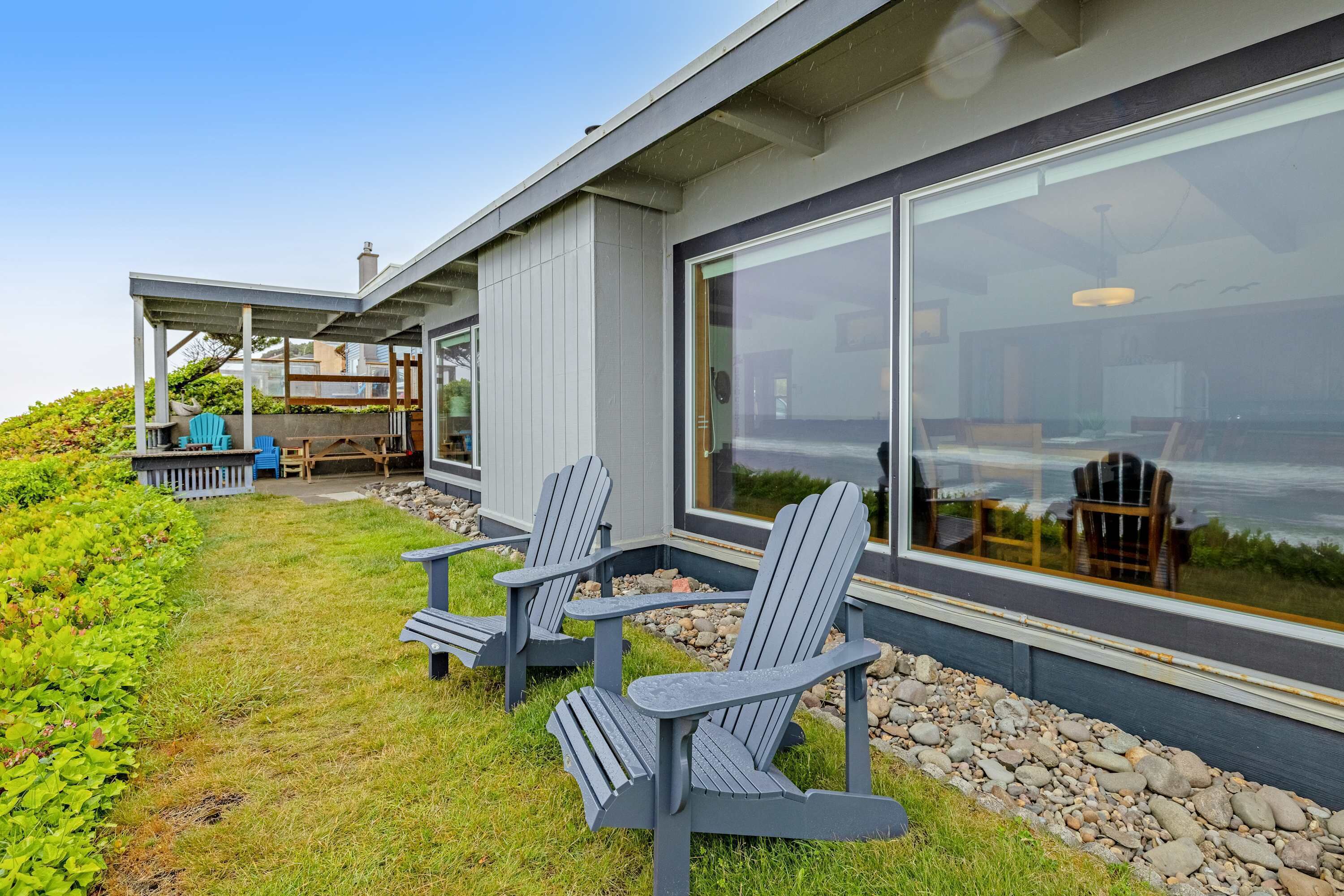 A modern house with a covered patio area featuring Adirondack chairs and a stone pathway.