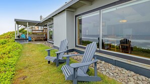 Een modern huis met een overdekte patio, Adirondack-stoelen en een pad van stenen.