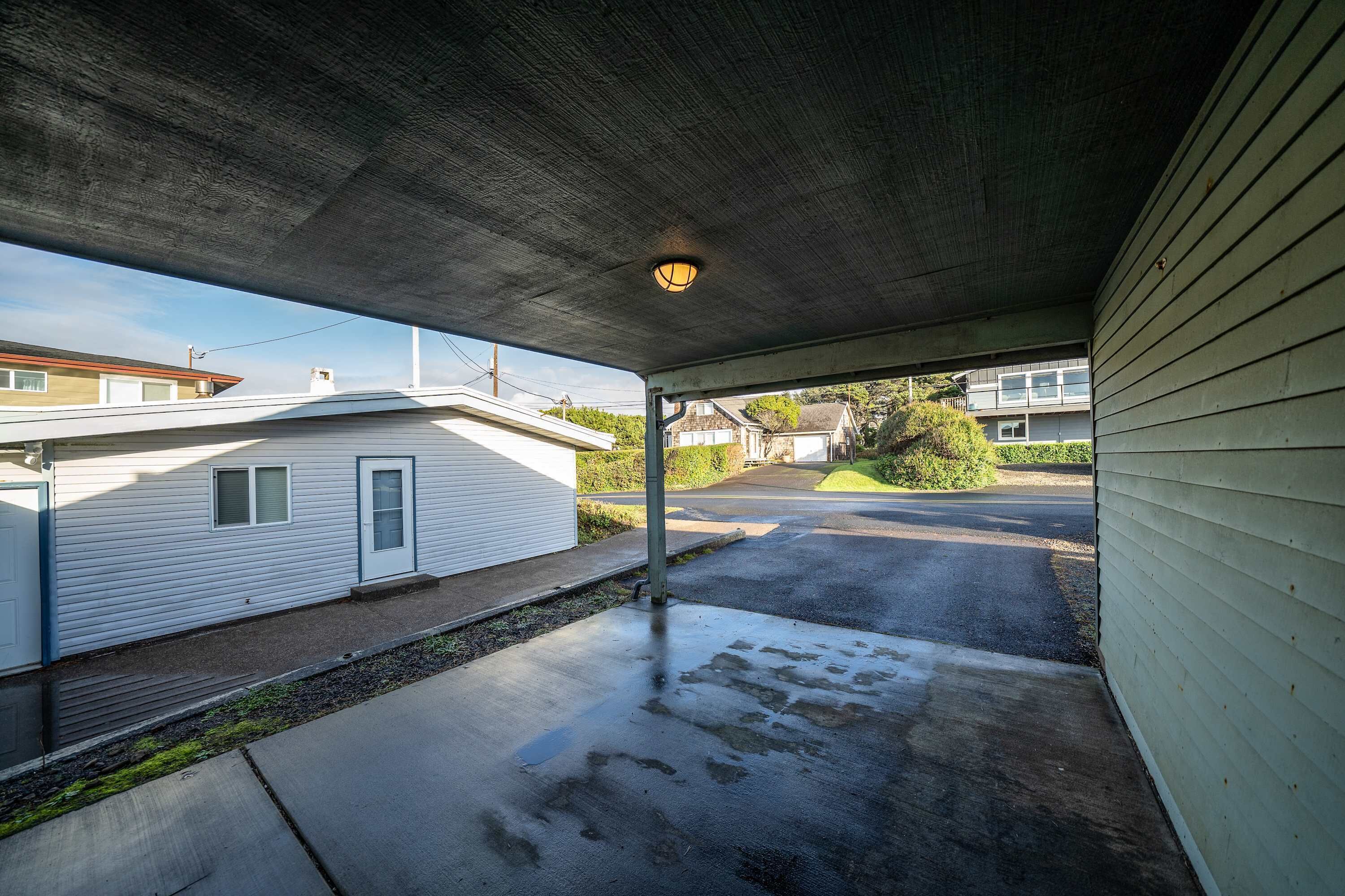 A covered outdoor area with a concrete floor, a lamp, and a view of a residential street.