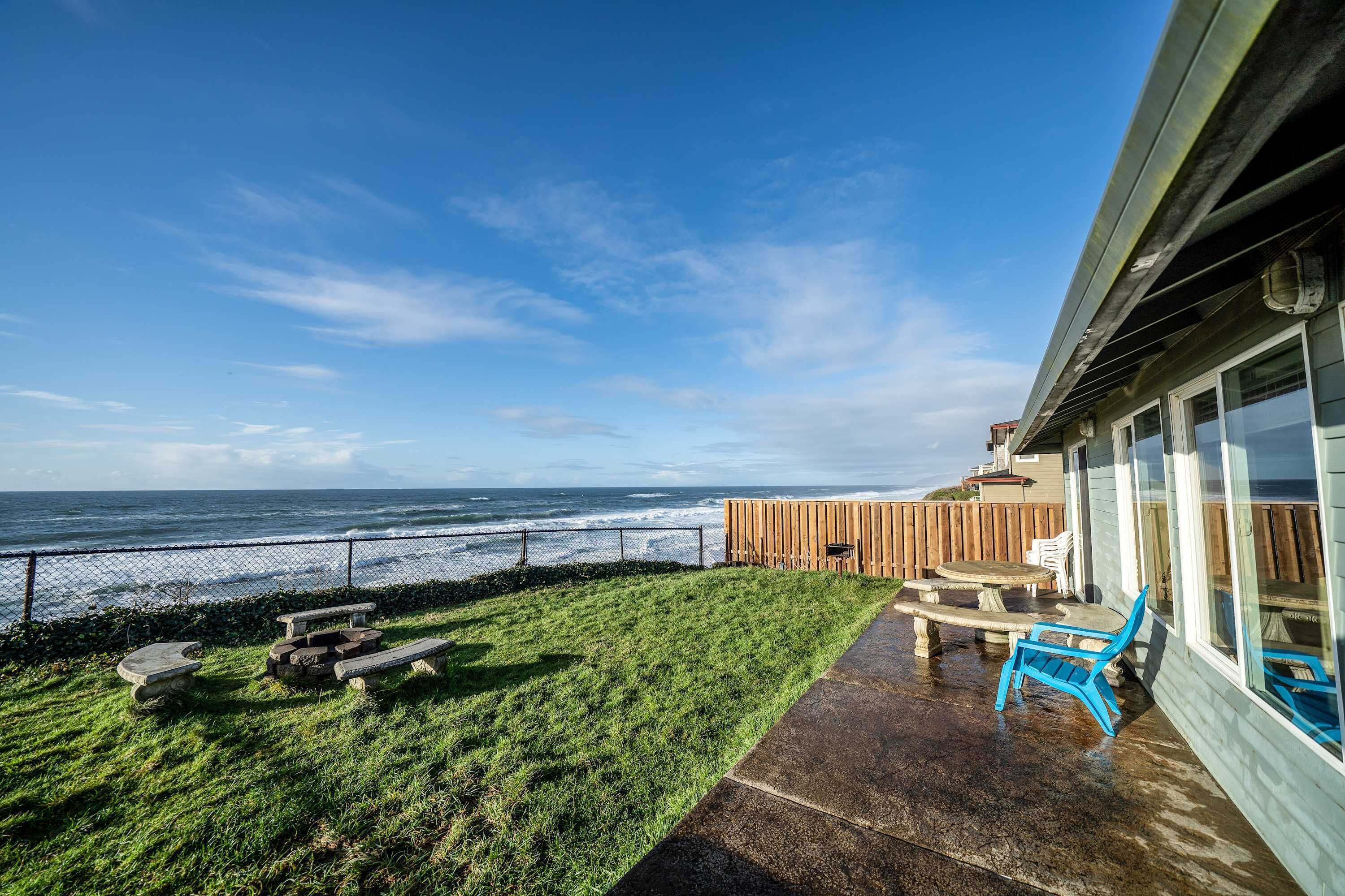 A patio with a view of the ocean, a wooden fence, and outdoor furniture.