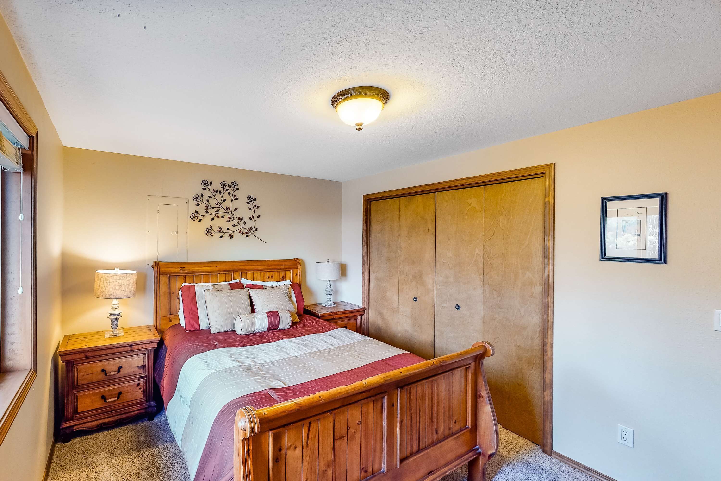 A bedroom with a wooden bed, nightstands, a wall-mounted light fixture, a wardrobe, and a framed picture on the wall.
