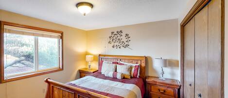Un dormitorio con cama de madera, una mesita de noche con lámpara, cómoda y armario.