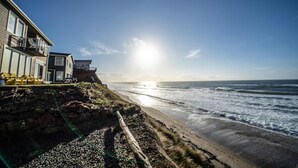 En fastighet vid kusten med utsikt över stranden, en träveranda och ett hus med en balkong.