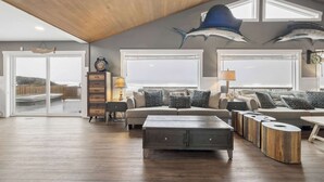Een ruime woonkamer met een grote bank, salontafel en decoratieve objecten. Twee grote ramen bieden uitzicht op de zee.