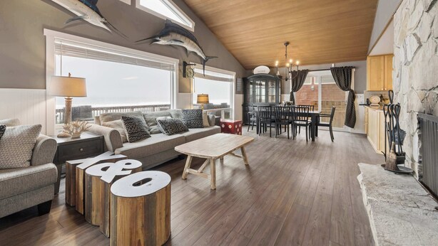 Een ruime woonkamer met houten plafond, een zithoek, een salontafel en een eethoek met tafel en stoelen.