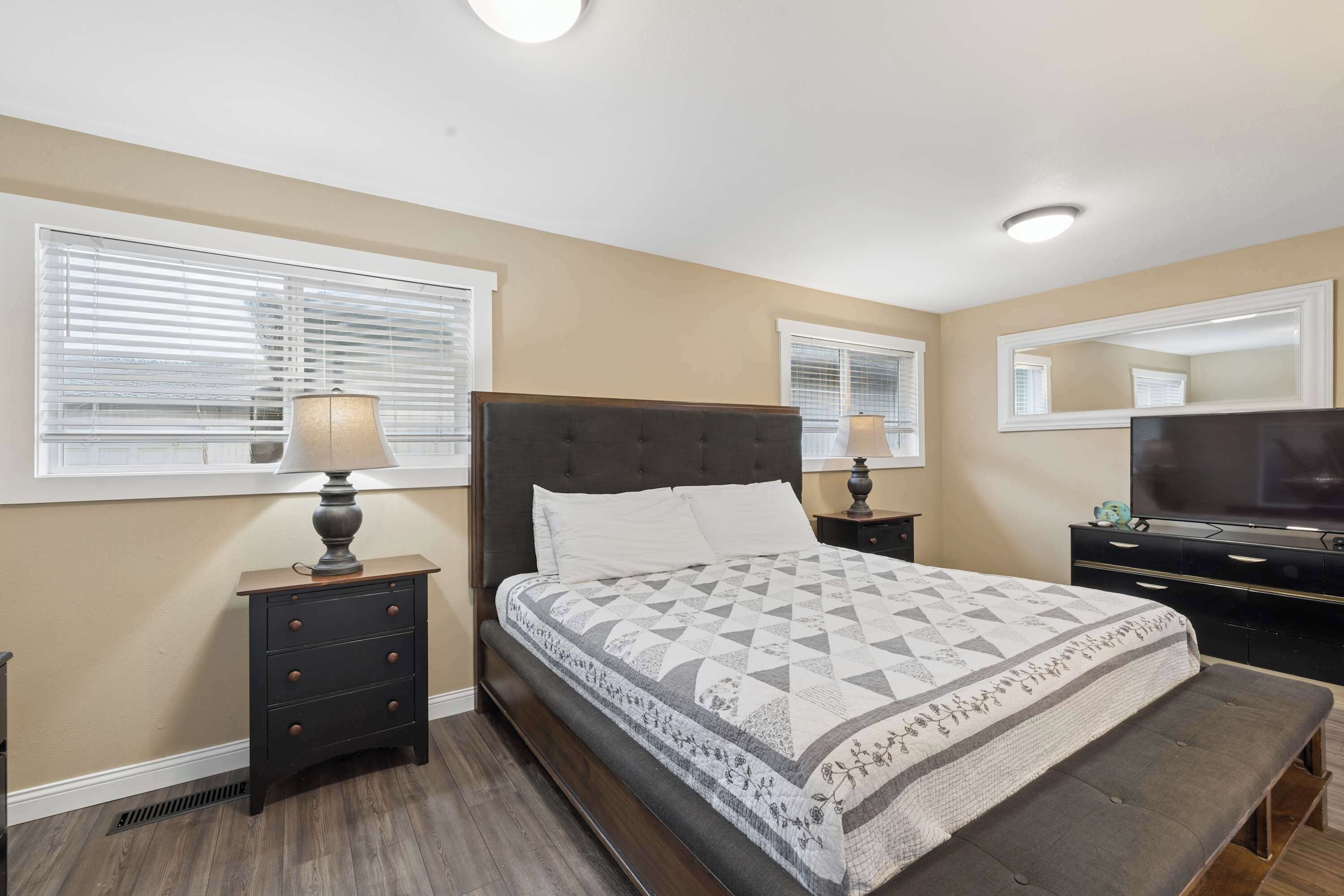 A bedroom with a bed, bedside tables, a lamp, a dresser, a mirror, and a television.