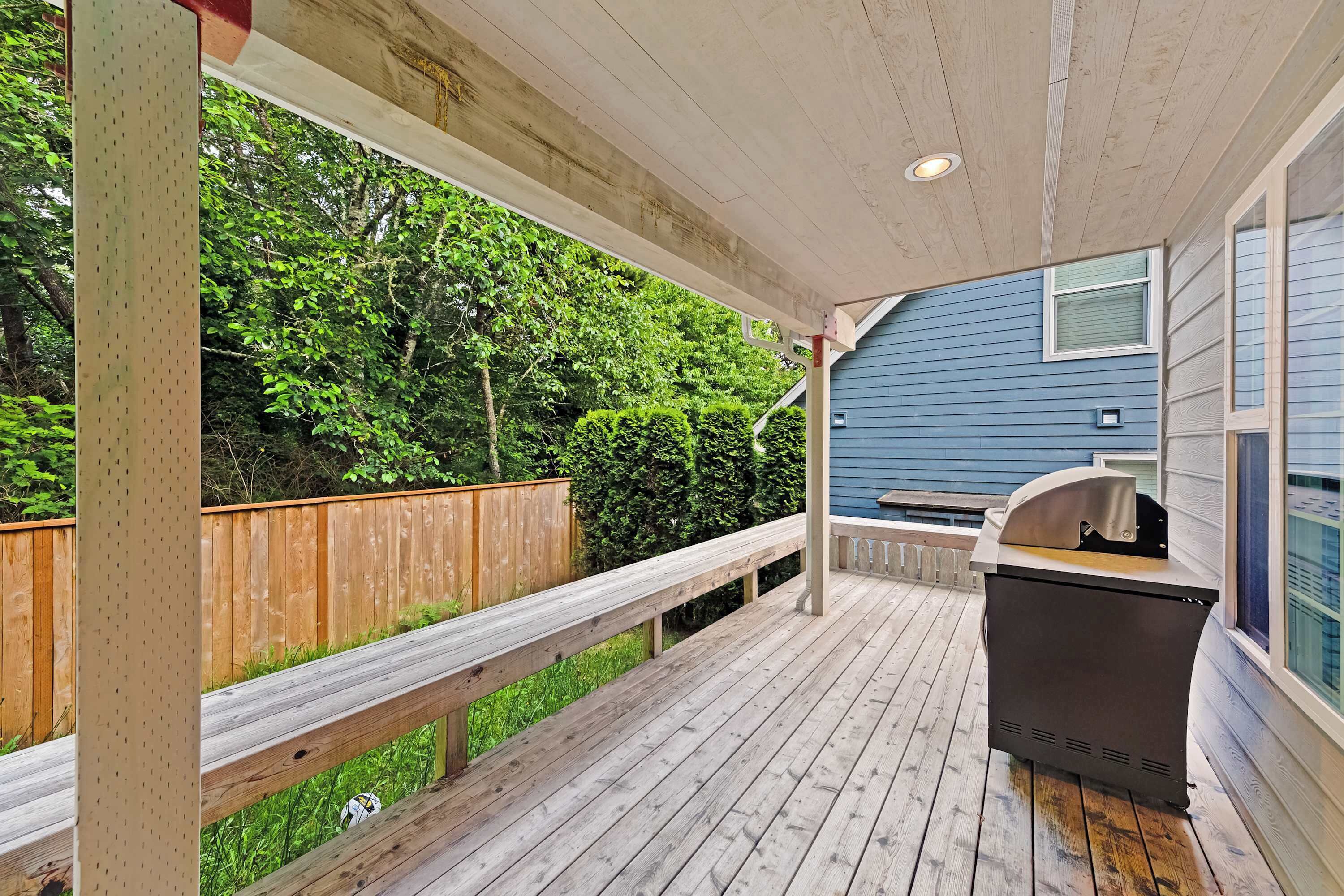 Une terrasse couverte avec un barbecue et vue sur une maison bleue.